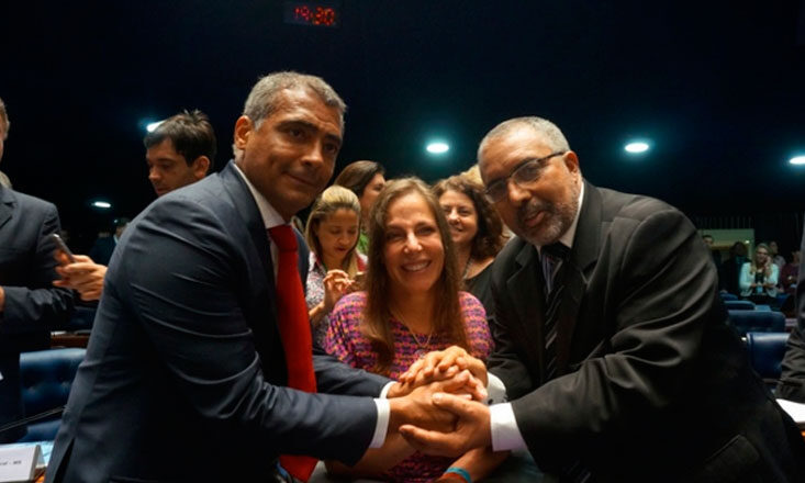 Romário, Mara Gabrilli e Paulo Paim se dão as mãos e sorriem para a câmera