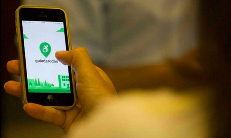 Uma mão segurando um telefone celular com a imagem de entrada do aplicativo Guia de Rodas