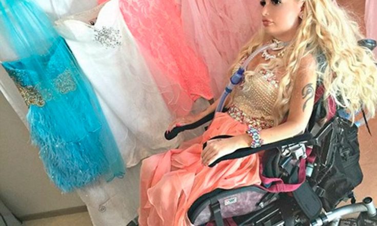 Garota em uma cadeira de rodas e um tubo respiratório na traquéia, vestida e maquiada como a boneca Barbie e, ao lado, vários vestidos
